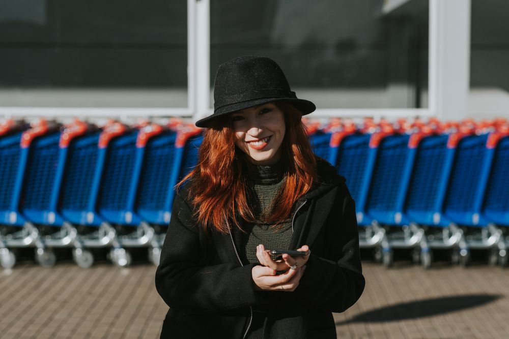 Smiling woman with smartphone in parking lot with shopping carts
