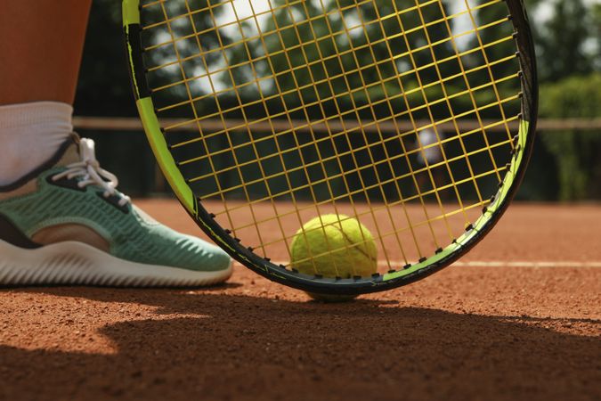 Woman leg, racket and tennis ball on clay court