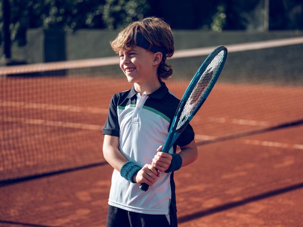 Cheerful adorable preteen boy in sportswear with tennis racket