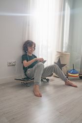 Positive preteen skater watching video on tablet in room