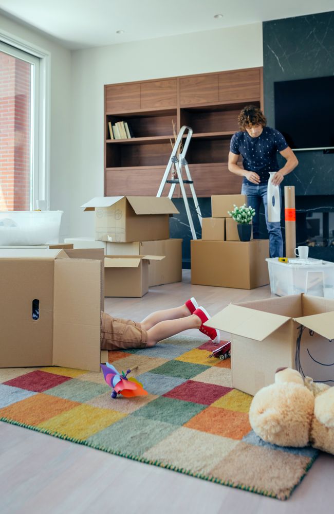 Boy playing inside a moving box while his father unpacks