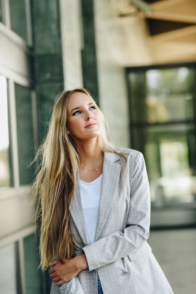 Woman in blazer looking up outside of building