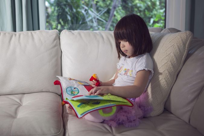 Girl holding children's book sitting on sofa