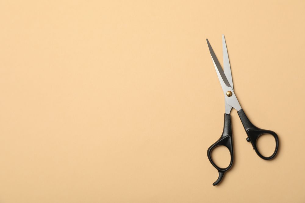 hairdresser scissors on beige background, space for text