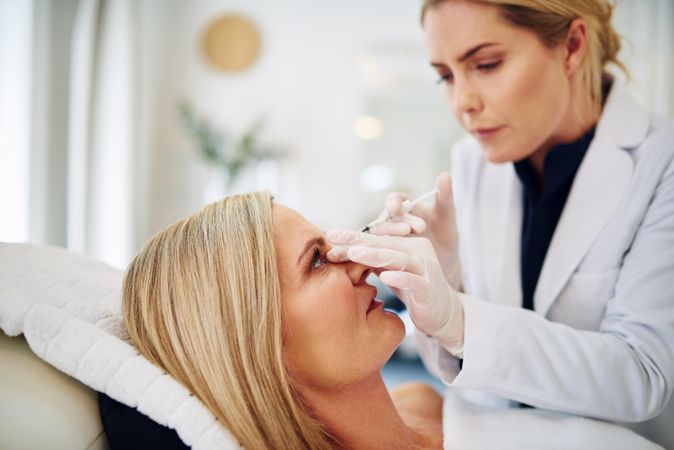 Side view of female dermatologist performing treatment on patient’s face