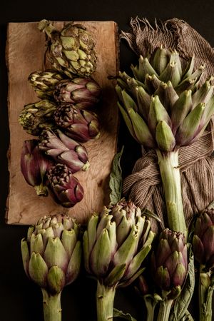 Fresh ripe artichokes placed on dark background with napkin and wooden table