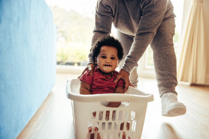 Young baby with afro smiling as his mother takes her for a ride in a basket at home