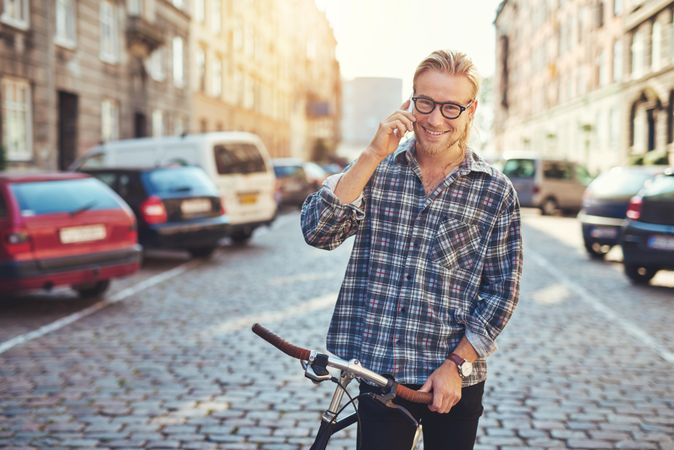 Man taking phone call on cobble street with bicycle