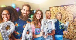 Smiling multi-ethnic friends holding balloons that say “party”