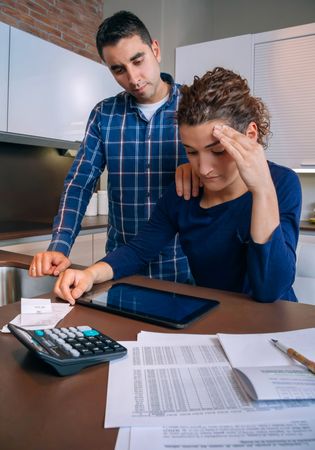 Stressed couple going through their bills together in the kitchen, vertical
