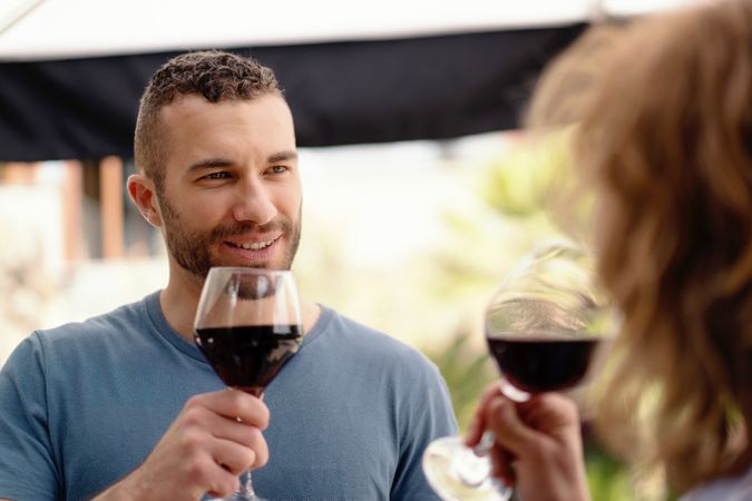 A man in sharp focus enjoys a glass of red wine, sharing a special moment with his partner