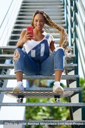 Happy female skater checking phone on stairs and playing with hair bYLgg4