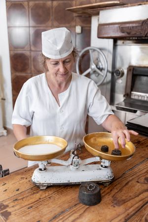 A baker woman weighing sugar with a weighing scales