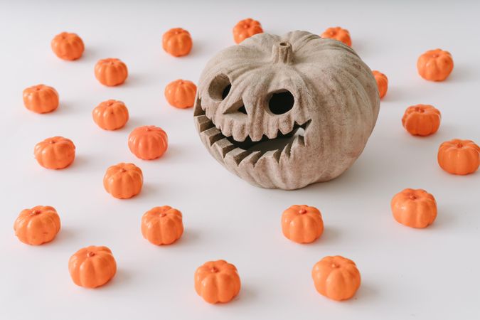 Pumpkin skull surrounded by mini orange pumpkins on light  background