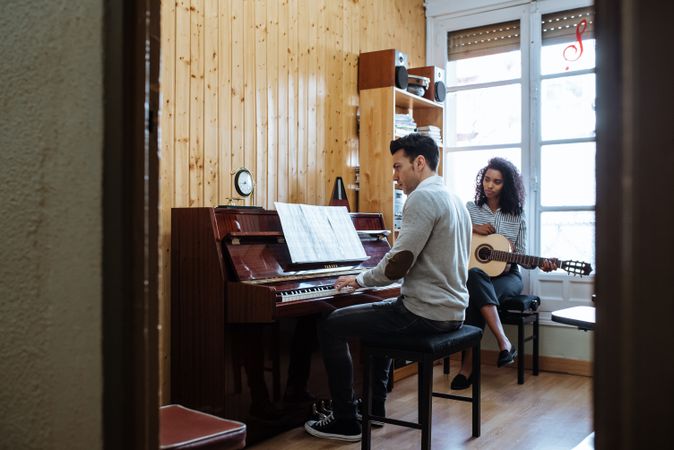 Man playing piano near woman playing guitar in studio