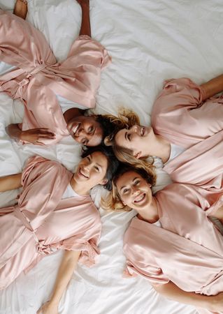 Top view of bride with bridesmaids lying on bed and smiling