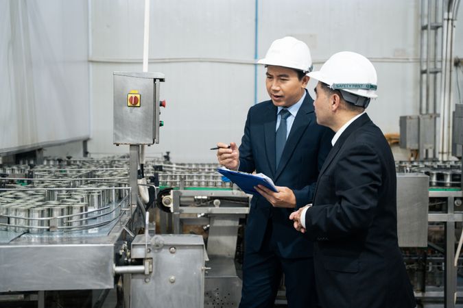 A businessman inspecting canned fish on conveyor belt at the factory