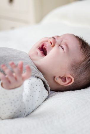 Baby girl crying over white bedcover