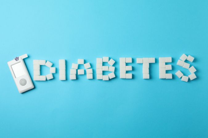 Diabetes made of sugar cubes and blood glucose meter on blue background
