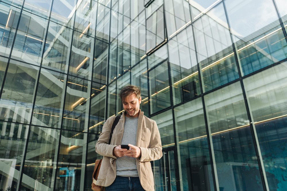 Smiling entrepreneur using smartphone outside office building