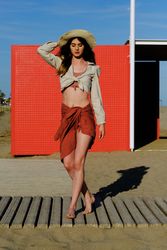 A long hair fashion model with a hat at the beach in front of a red wall