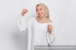 Giddy Muslim woman in headscarf in light blouse with hands up in celebration 4dwnE5