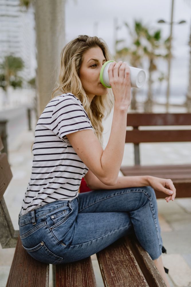 Happy woman with disposable cup of coffee sitting on street bench