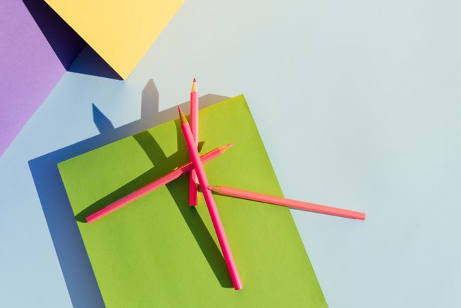 Pink pencils on green book, in space of geometric shapes.