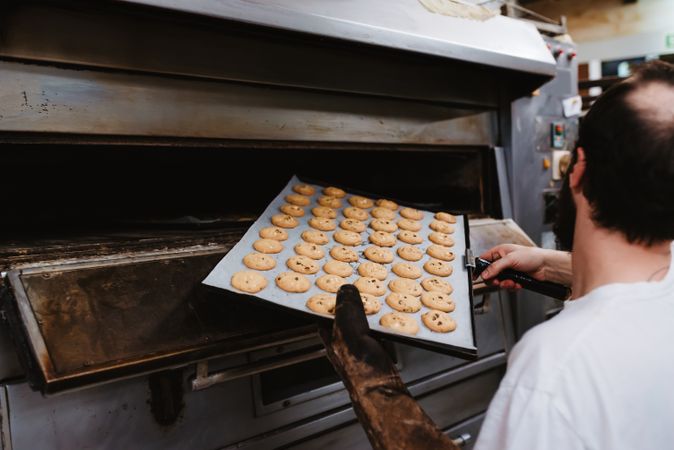 Bald baker checking pastry inside oven