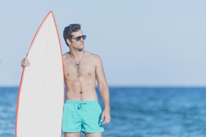 Male surfer standing with red outlined board on seashore