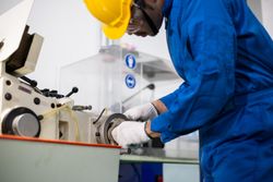 Male in blue jumpsuit and PPE gear operating machinery in manufacturing factory
