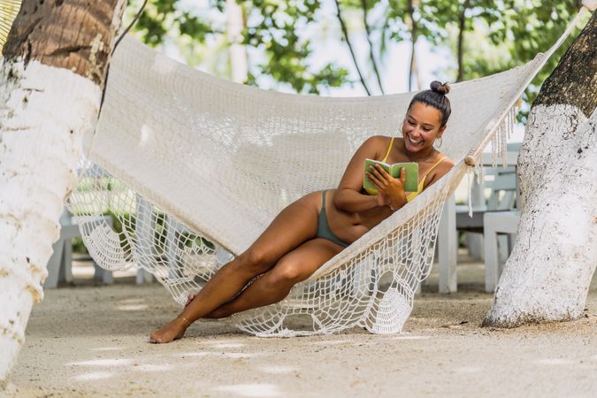 Joyful woman in bikini resting in hummock on beach
