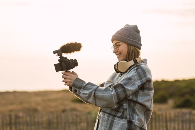 Happy female recording vlog on camera under sundown sky