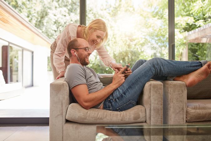 Man sitting on sofa with woman standing by standing behind looking at tablet