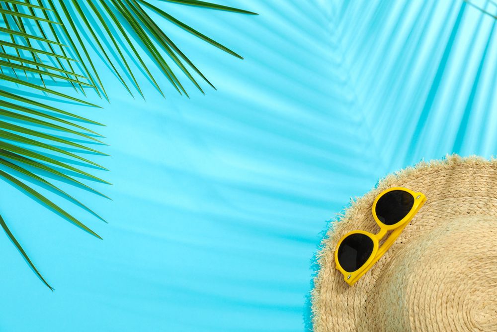 Palm leaves, straw hat and sunglasses on color background, space for text. Summer vacation backdrop