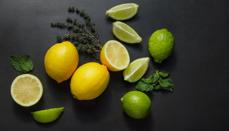 Cut and uncut limes and lemons on a dark background along with mint leaves