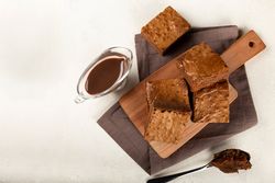 Top view of chocolate brownies served on wooden board with pot of syrup on the side