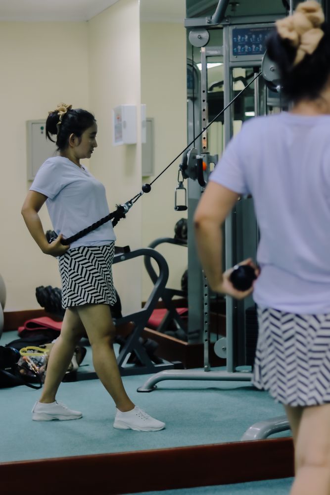 A woman uses a cable machine in a gym, doing an exercise routine