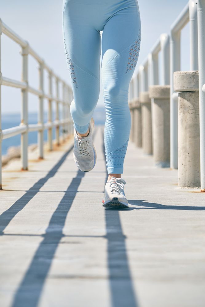 Crop jogger running on bridge over sea during cardio training