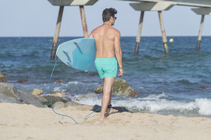 Male surfer with blue board approaching the coast