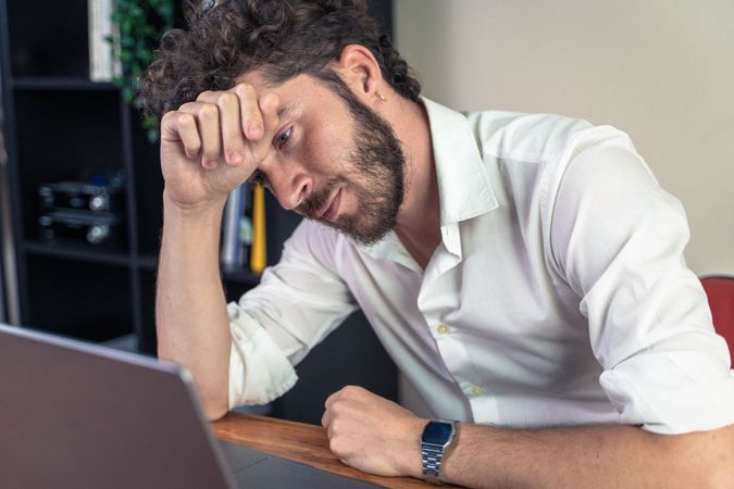 Stressed young man feeling burnout while working on a laptop.