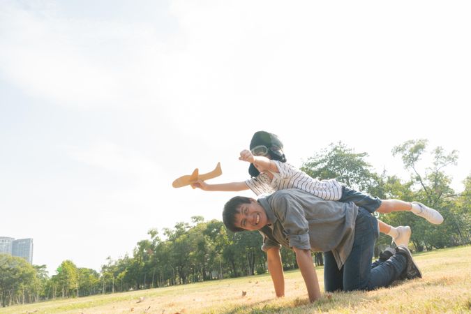 Son on father’s back back and playing with toy plane in public park