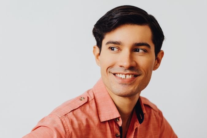 Headshot of smiling Hispanic male looking away in grey studio, copy space