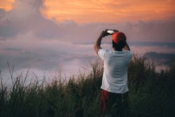 Back view of man standing on highland taking photo of the sunset horizon above the cloud