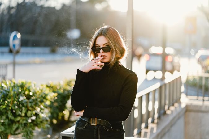 Stylish woman lighting cigarette near metro station