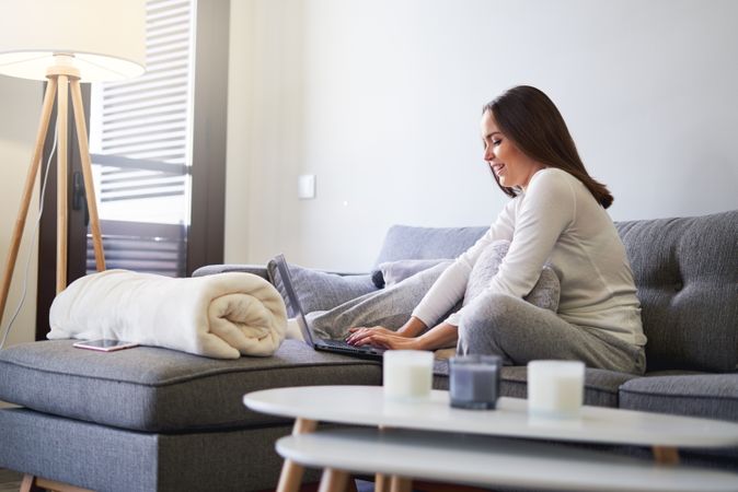 Smiling woman browsing on laptop and sitting on settee