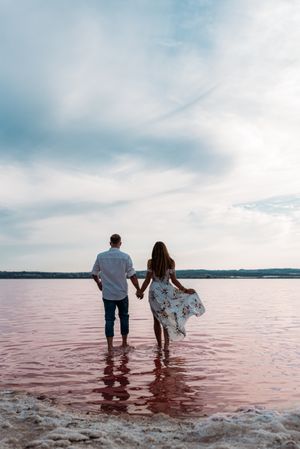back view of adorable couple going into an amazing beach with pink water