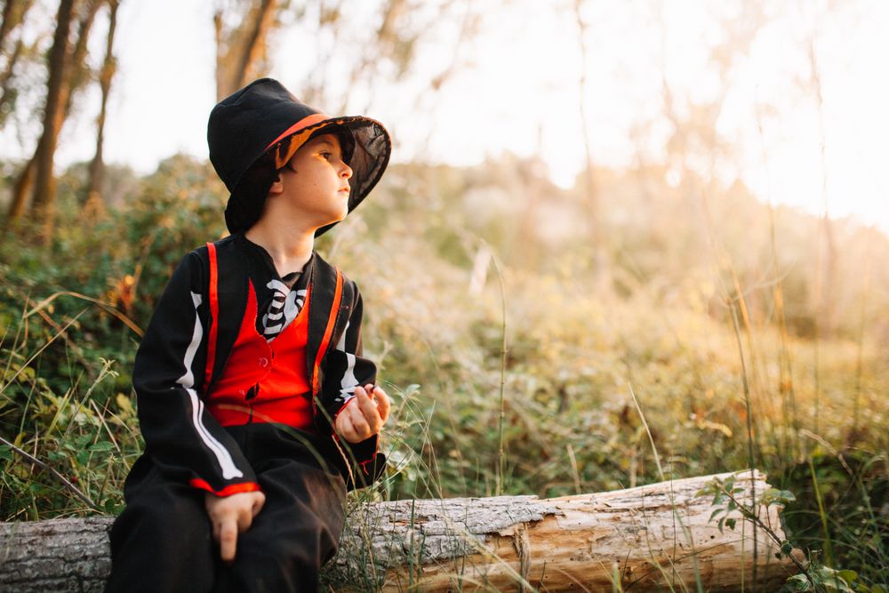 Boy in skeleton costume looking off in the distance while sitting on a log