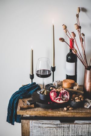 Rustic setting of wine, cheese, long candles, with pomegranate, and dried poppies