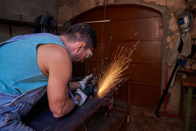 Man cutting metal standing at workbench and using disk grinder